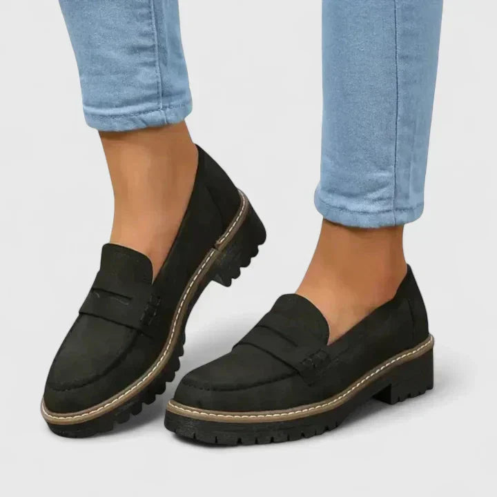 Black loafers worn with light blue jeans on a plain background