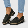 Black loafers worn with light blue jeans on a plain background